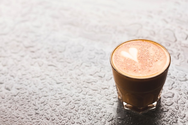 Latte chaud avec forme de coeur en verre sur la surface de la goutte d&#39;eau