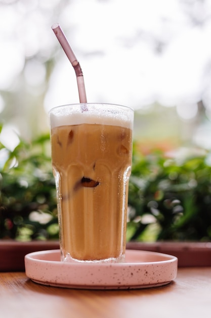 Latte glacé en verre sur un support rose sur une table en bois en été café buissons verts