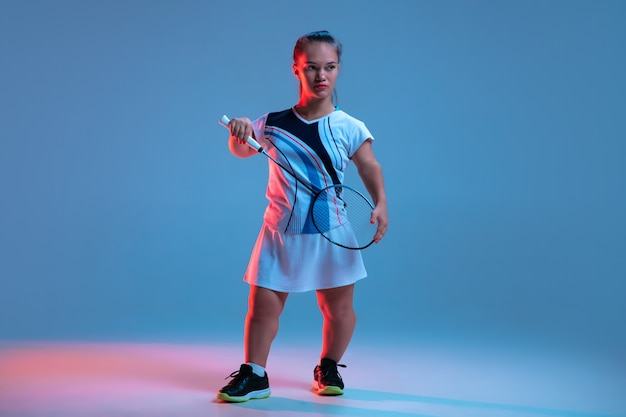 Leader. Belle petite femme pratiquant le badminton isolée sur bleu à la lumière du néon. Mode de vie des personnes inclusives, diversité et équité