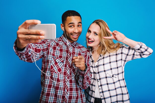 Élégant beau mec faisant portrait de selfie avec jolie jeune femme aux longs cheveux blonds. S'amuser, écouter de la musique avec des écouteurs, bonne humeur, se détendre.