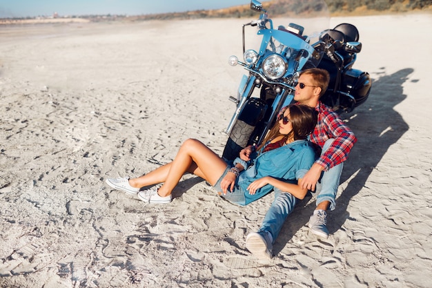 Élégant couple amoureux posant près de vélo sur la plage ensoleillée.