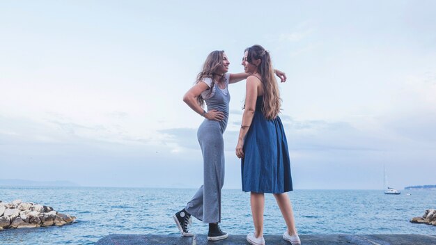 Élégant deux jeunes amies debout contre le ciel et la mer bleue