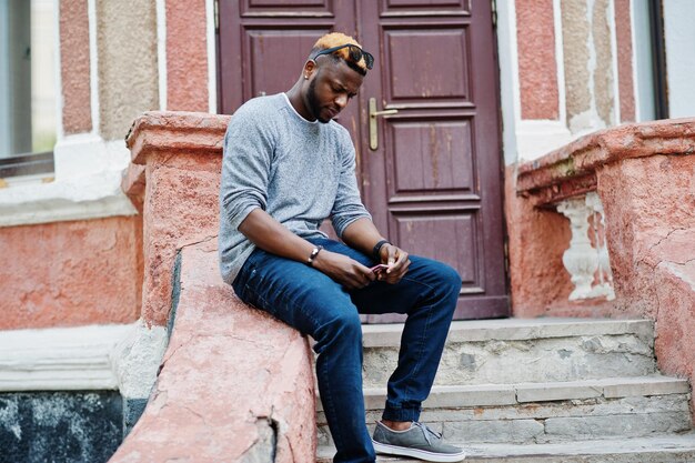 Élégant garçon afro-américain sur pull gris et lunettes de soleil noires posées dans la rue