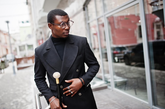 Élégant gentleman afro-américain dans une élégante veste noire tenant un bâton de marche rétro comme flacon de canne ou canne basculante avec poignée en boule de diamant doré Riche homme afro à la mode