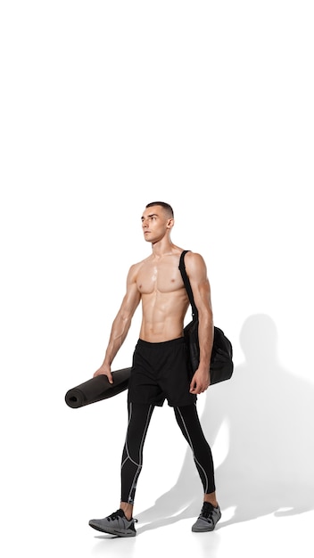 Élégant jeune athlète masculin pratiquant sur fond de studio blanc, portrait avec des ombres. Modèle de coupe sportive en mouvement et en action. Body building, mode de vie sain, concept de style.