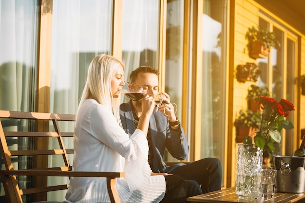 Élégant jeune couple assis dans le patio, boire du vin rouge