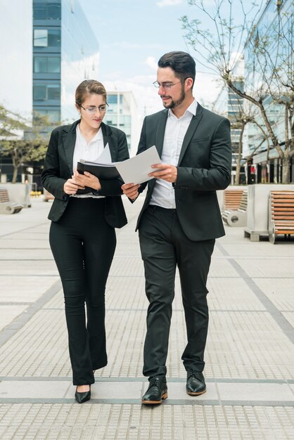 Élégant jeune homme d&#39;affaires et femme d&#39;affaires en regardant le document tout en marchant sur le trottoir