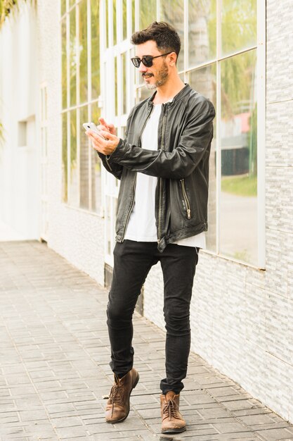 Élégant jeune homme debout sur le trottoir à l&#39;aide de smartphone