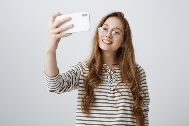 Élégante adolescente prenant selfie sur smartphone, souriant heureux