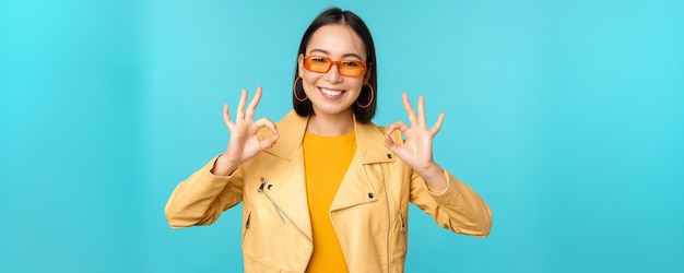 Élégante belle femme asiatique à lunettes de soleil souriant étonné montrant bon signe ok recommandant smth su