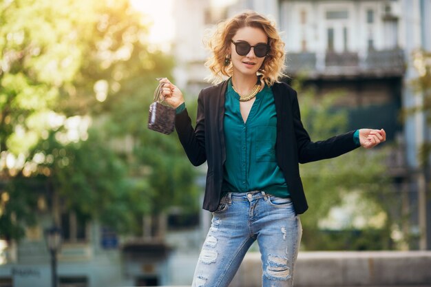 Élégante belle femme en jeans et veste marchant dans la rue avec petit sac à main, style élégant, tendances de la mode printanière