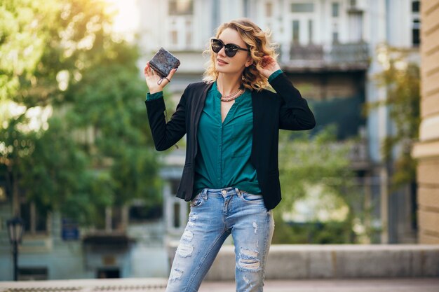 Élégante belle femme en jeans et veste marchant dans la rue avec petit sac à main, style élégant, tendances de la mode printanière