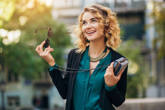 Élégante belle femme en jeans et veste marchant dans la rue avec petit sac à main, style élégant, tendances de la mode printanière