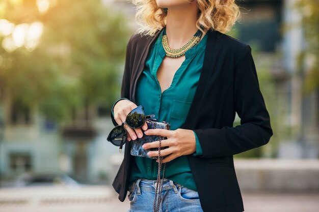 Élégante belle femme en jeans et veste marchant dans la rue avec petit sac à main, style élégant, tendances de la mode printanière