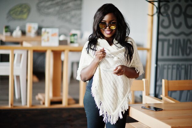 Élégante fille afro-américaine à lunettes de soleil posée au café moderne et manger de la crème glacée