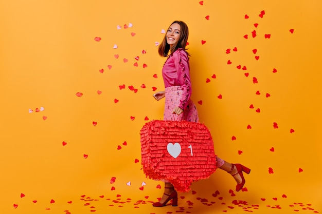 Élégante fille attrayante posant avec un sourire inspiré. Blogueuse Jocund en blouse rose riant sous des confettis.