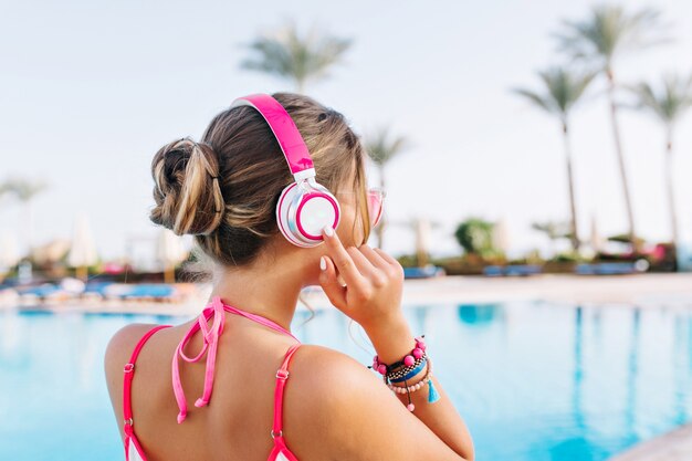 Élégante fille bronzée avec une coiffure mignonne debout devant la grande piscine extérieure prête à nager en matinée ensoleillée