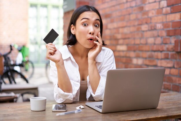 Élégante jeune femme asiatique faisant des achats en ligne assis avec carte de crédit et ordinateur portable achetant en stagiaire