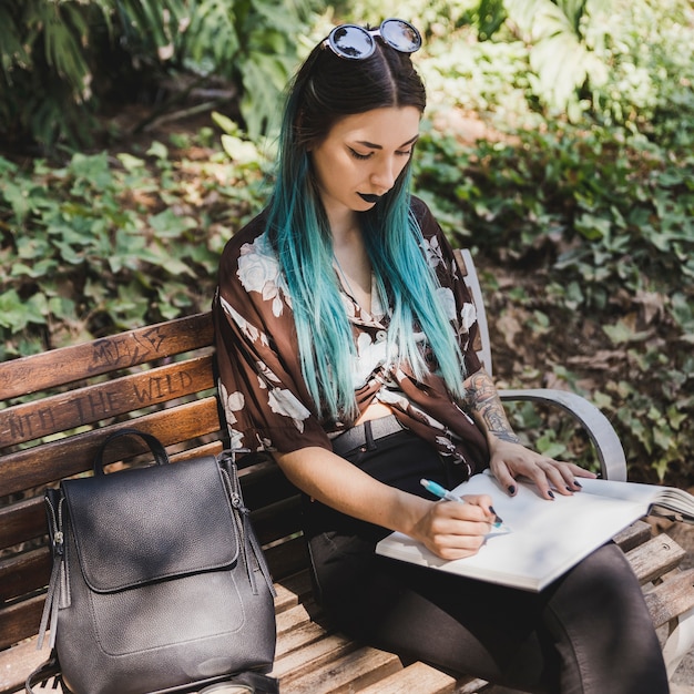 Élégante jeune femme assise sur un banc écrit sur un cahier avec un stylo