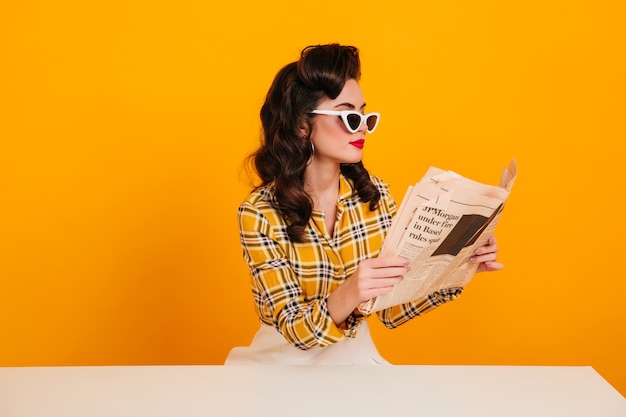 Élégante jeune femme lisant le journal. Photo de Studio de pin-up concentré posant sur fond jaune.