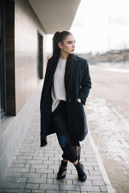 Élégante jeune femme en manteau avec foulard dans la rue