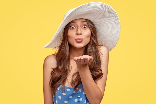 Élégante jeune femme portant un chapeau posant contre le mur jaune