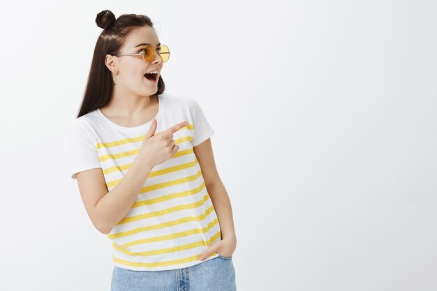 Élégante jeune femme posant avec des lunettes de soleil contre le mur blanc