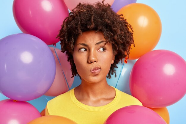 Élégante jeune femme réfléchie posant entourée de ballons colorés d'anniversaire