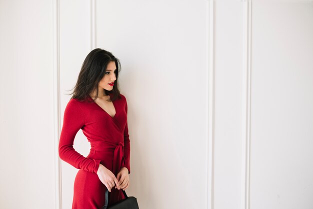 Élégante jeune femme en robe rouge avec sac à main dans la chambre