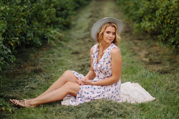 Élégante jeune femme en robe vintage rose bleu et chapeau posant dans le champ vert