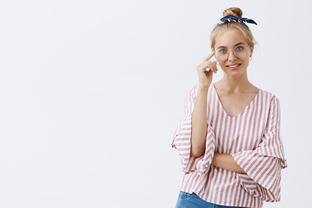 Élégante jeune fille blonde moderne posant contre le mur blanc