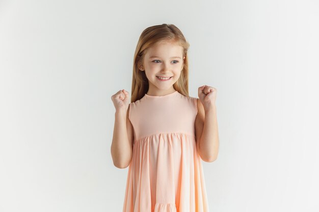 Élégante petite fille souriante posant en robe isolée sur un espace blanc. Modèle féminin blonde caucasienne. Émotions humaines, expression faciale, enfance