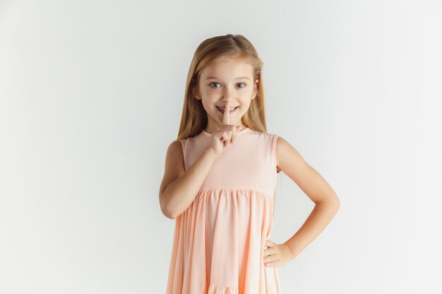 Élégante petite fille souriante posant en robe isolée sur un espace blanc. Modèle féminin blonde caucasienne. Émotions humaines, expression faciale, enfance