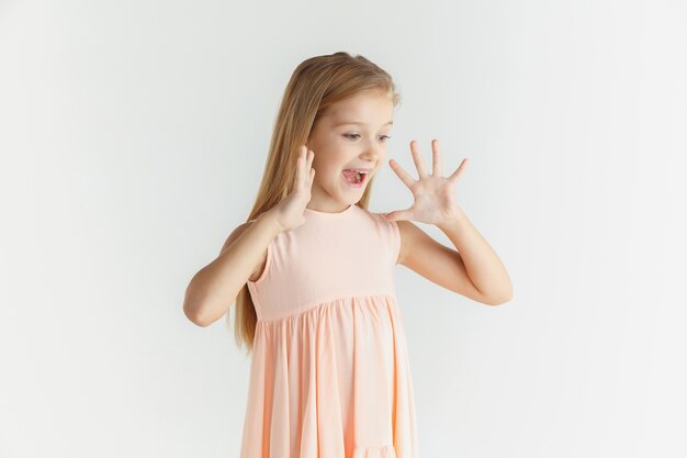 Élégante petite fille souriante qui pose en robe isolée sur studio blanc