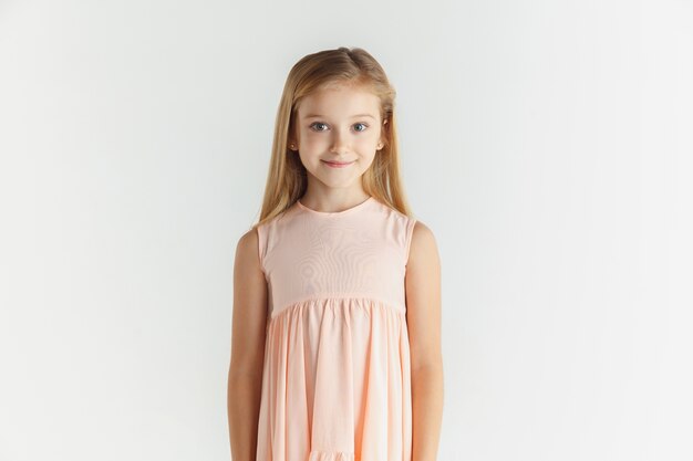 Élégante petite fille souriante qui pose en robe isolée sur studio blanc