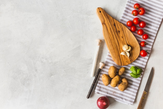 Des légumes; éprouvettes de sel et de poivre noir et planche à découper sur une serviette sur fond blanc