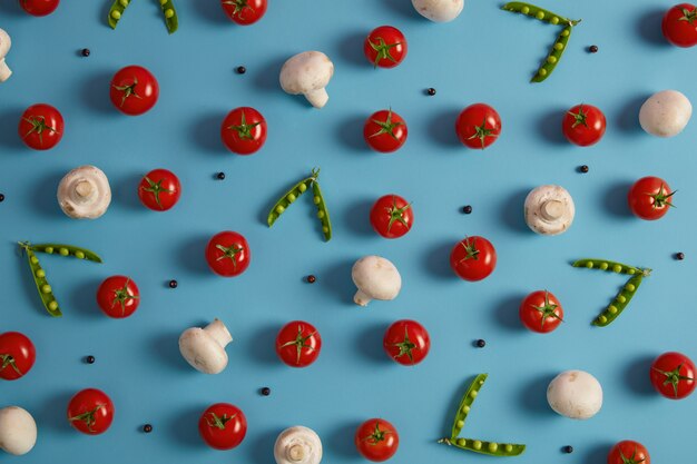 Légumes frais, ingrédients pour cuisiner une soupe ou une salade. Champignons, tomates rouges, pois verts et grains de poivre sur fond bleu. Alimentation saine, produits nutritifs. Mise au point sélective, au-dessus de la photo