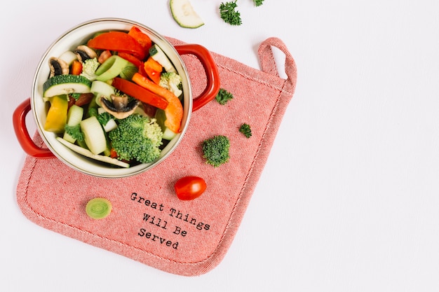 Légumes frais non cuits dans une marmite sur un napperon sur fond blanc