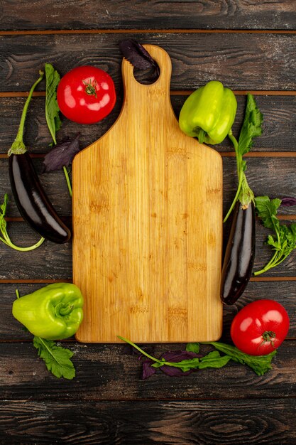 Légumes frais une vue de dessus des aubergines noires riches en vitamines mûres tomates rouges et poivrons verts avec des herbes vertes sur un bureau en bois rustique