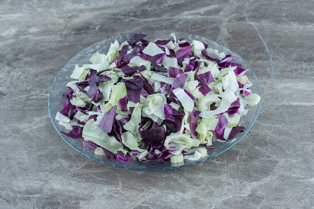 Légumes hachés dans le bol en verre, sur la table en marbre.