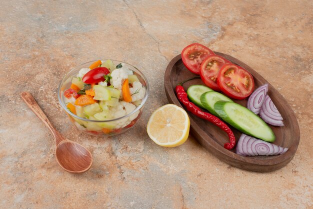 Légumes savoureux sur plaque de verre avec planche de bois de tomate, concombre et oignon sur marbre