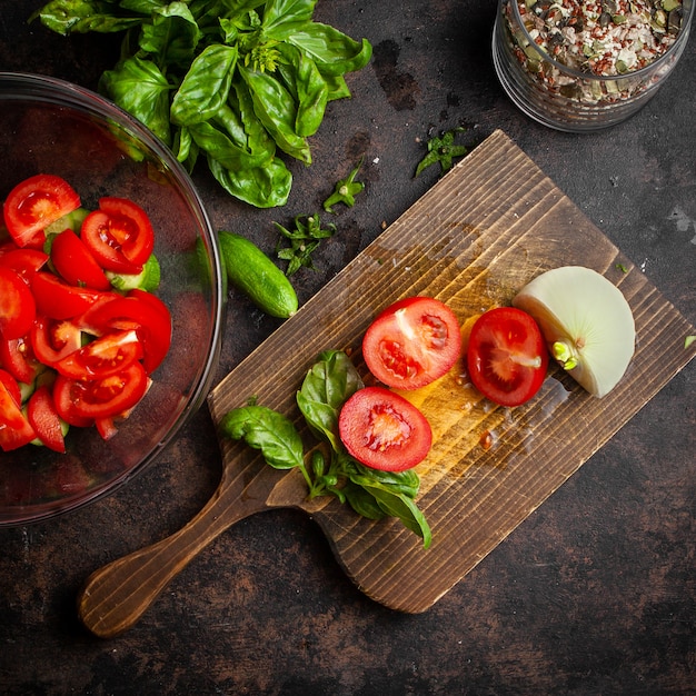 Légumes en tranches dans un bol en verre de tomates, concombres avec pot de céréales, oignon et épinards vue de dessus sur une planche sombre et à découper