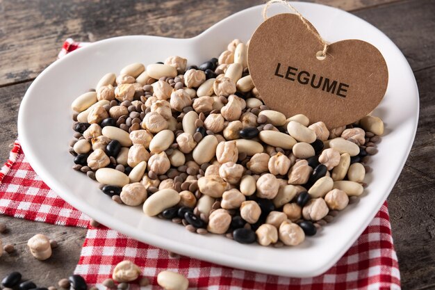 Légumineuses assorties non cuites dans une assiette en forme de coeur sur une table en bois rustique