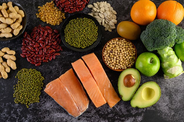 Légumineuses, brocoli, fruits et saumon placés sur un sol en ciment noir.