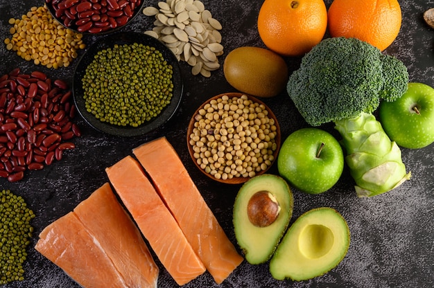 Légumineuses, brocoli, fruits et saumon placés sur un sol en ciment noir.