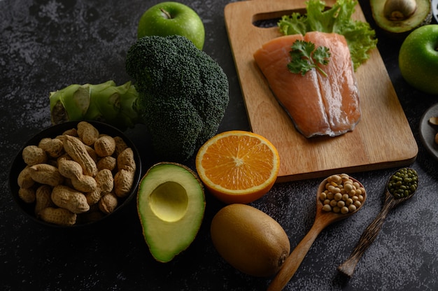 Légumineuses, fruits et morceaux de poisson saumon sur une planche à découper en bois.