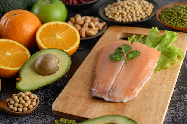 Légumineuses, fruits et morceaux de poisson saumon sur une planche à découper en bois.