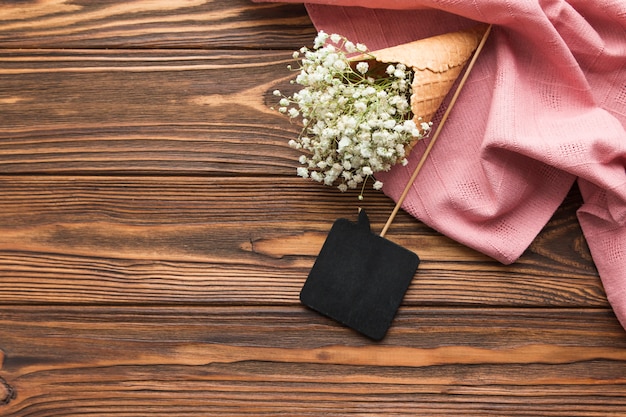 Élément de discours noir et gypsophile à l&#39;intérieur du cornet de crème glacée sur un textile rose sur un fond texturé en bois