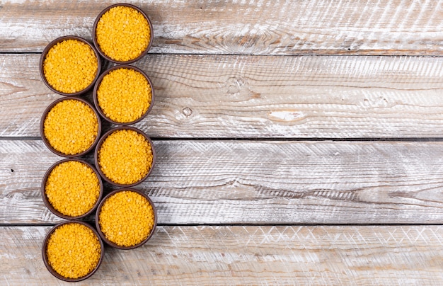 Lentilles jaunes dans un bol brun plat posé sur une table en bois beige avec fond