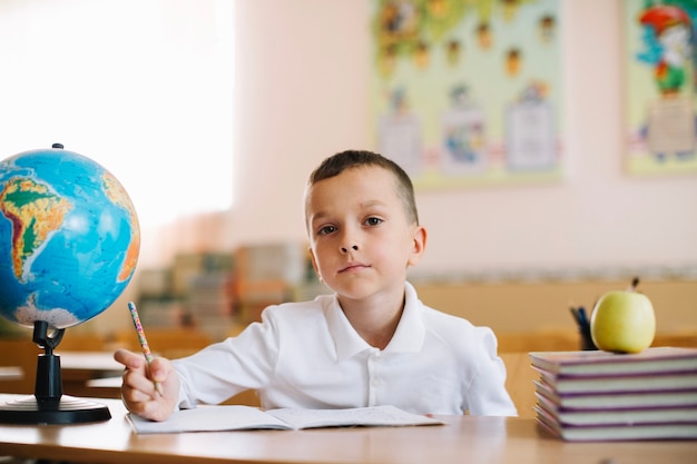 Élève réfléchi avec globe sur le bureau